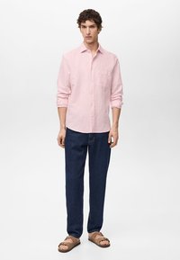 Lichtroze overhemd met lange mouwen, een borstzak, gecombineerd met donkerblauwe jeans en bruine sandalen. Eenvoudig ontwerp en casual pasvorm.