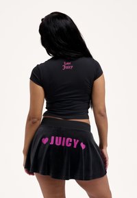 Μαύρο κοντομάνικο μπλουζάκι με ροζ κείμενο «Love Juicy» στην πλάτη, σε συνδυασμό με μαύρη βελουτέ φούστα με μεγάλο ροζ γράμμα «JUICY» και καρδιές ως διακοσμητικά στοιχεία.