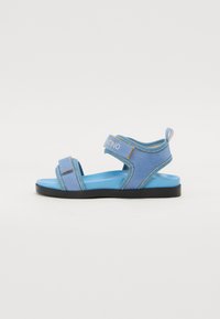 Blauwe sandalen met een zachte bovenkant, verstelbare banden en een gevoerde voetbed. Kenmerkt een contrasterende donkere zool en branding op de band.