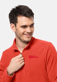 Pullover in pile rosso con colletto a mezza zip, caratterizzato da un logo sull'area sinistra del petto e un tessuto morbido e texturizzato.