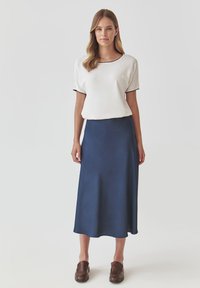 White short-sleeve top with black trim paired with a long navy skirt, smooth fabric, and brown slip-on shoes. Simple and elegant silhouette.