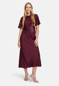 Completo bordeaux composto da un top a maniche corte con paillettes e una gonna liscia e fluente. Sandali alti argentati completano il look.