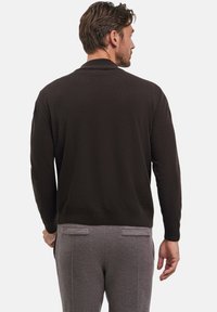 Cardigan a maglia marrone scuro con colletto e polsini a coste, con maniche lunghe. Abbinato a pantaloni eleganti grigi chiari.