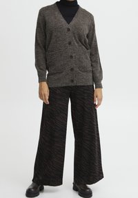 Brun stickad kofta med v-ringning, knappstängning och två framfickor. Matchas med vida byxor med ett mönster av mörka tigerränder.