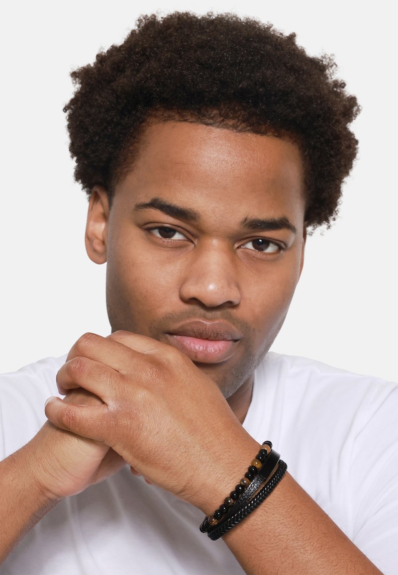 Bracciali neri con varie trame, tra cui perline lisce e design intrecciati, indossati su un polso, su uno sfondo chiaro.