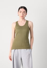 Oliven grønn tank top med ribbestruktur, med en dekorativ detalj ved utringningen. Kombinert med lys grå vide sweatpants.