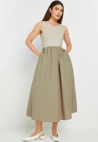 Ärmelloses Kleid mit einem taillierten, hellbeigen Oberteil und einem fließenden, gerafften, khakifarbenen Rock. Verfügt über Taschen und eine lange A-Linien-Silhouette.