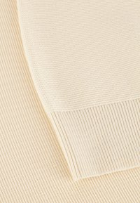 Crème-kleurige gebreide stof met ribbelstructuur. Close-up weergave van de gebogen rand en duidelijke patronen die ontstaan door het stikken.