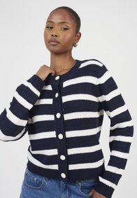 Cardigan rayé bleu marine et blanc en tissu tricoté. Doté d'un col rond, de manches longues et de grands boutons ronds le long de l'avant.