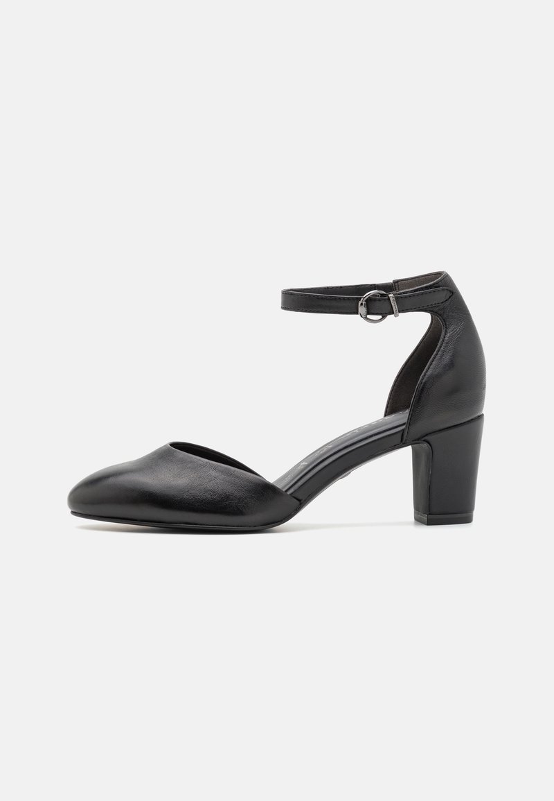 Chaussure en cuir noir à talon moyen avec bout pointu fermé et bride de cheville avec boucle argentée sur fond blanc.