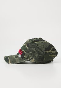 Camo groene baseballpet met zwart en beige patronen en rode geborduurde tekst op het voorpaneel, van opzij bekeken op een witte achtergrond.