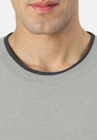 Maglione grigio chiaro a girocollo con tessuto strutturato. Presenta un colletto a coste di colore blu scuro. Vista ravvicinata che mostra l'area del collo e i dettagli del tessuto.