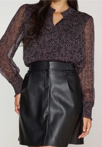Blouse noire transparente à manches longues avec motif floral rose ; associée à une jupe noire en similicuir avec des boutons à l'avant et une taille haute.
