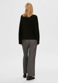 Pull noir surdimensionné avec ourlet côtelé associé à un pantalon à motif pied-de-poule gris. La personne porte des cheveux à hauteur des épaules.
