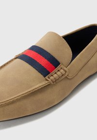 Beige semskede loafers med et marineblått og rødt stripet tekstilbånd over toppen. Har dekorativ søm og en rund tådesign.