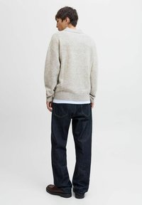 Lys grå strikket sweater med ribbestrikket kant og manchetter, parret med mørkeblå jeans og sorte sko. Synlig syning og tekstureret stof.