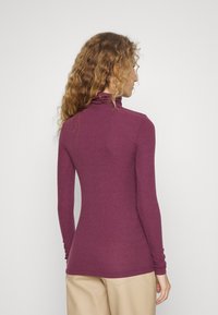Lange mouwen coltrui in diep paars, ribbeltextuur, aansluitend ontwerp. Gezien vanaf de achterkant, gecombineerd met lichtgekleurde broek.
