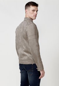 Jachetă de motor din suede gri, cu un design ajustat, prezentând accente de umăr ribbate și o textură netedă, asociată cu blugi negri.
