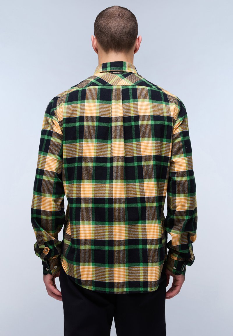 Chemise à carreaux avec des couleurs vertes, jaunes, noires et brunes. Elle a des manches longues, un col, et des boutons aux poignets, avec un ourlet arrondi.