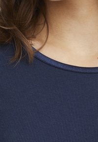 Námořnická pruhovaná látka s kulatým výstřihem a kontrastní tmavě modrou lemovkou. Detailní záběr ukazující texturu a designové detaily na oděvu.