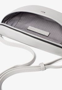 White leather crossbody bag with a zip closure. Interior features a herringbone pattern in black and white. Adjustable strap included.
