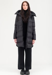 Doudoune noire avec capuche, fermeture éclair à l'avant et couture horizontale. Assortie à un col roulé noir et à un pantalon ample. Tissu texturé.