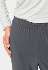 Grijze stretchbroek met een elastische tailleband, een gladde textuur en zijnaaddetails, gecombineerd met een witte langwerpige top.