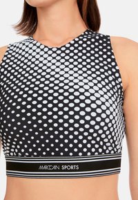 Black and white cropped sports top with a polka dot pattern, featuring a high neckline and a branded elastic waistband. Smooth texture.