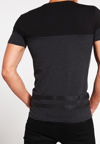 Černé a tmavě šedé tričko s krátkým rukávem, kulatým výstřihem a horizontálním panelem na horní části zad a na spodním lemu.