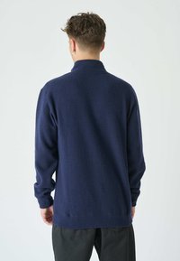Marineblauer Fleece-Pullover mit hohem Kragen, langen Ärmeln und elastischen Bündchen. Weiche Textur mit lockerer Passform, mit geradem Saum an der Taille.