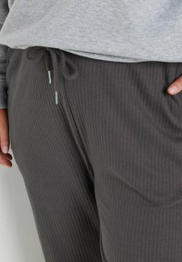 Grijze geribde joggingbroek met een elastische tailleband en trekkoord. De stof lijkt zacht, gestructureerd en licht rekbaar.