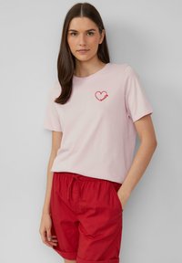 Lichtroze katoenen T-shirt met een rode hartafbeelding en het woord "omdat" eronder, gecombineerd met rode shorts met een trekkoord.