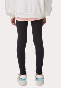 Svarta leggings i kombination med en vit oversized sweatshirt och färgglada sneakers. Leggingsen är åtsittande med en jämn textur.