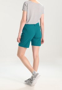 Turkosa shorts i lättviktigt material, med en slank design och en bakficka. Matchas med en ljusgrå t-shirt och träningsskor.