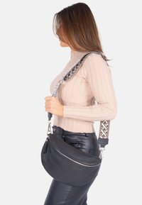 Schwarze Leder-Hobo-Tasche mit geschwungener Form, ausgestattet mit einem gemusterten verstellbaren Träger. Ein Reißverschluss und eine glatte Textur sind hervorzuhebende Details.