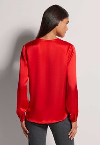 Rode zijden blouse met lange, opgezette mouwen; gladde textuur; ronde halslijn; subtiele glans; gebogen zoom; aansluitend op de taille.