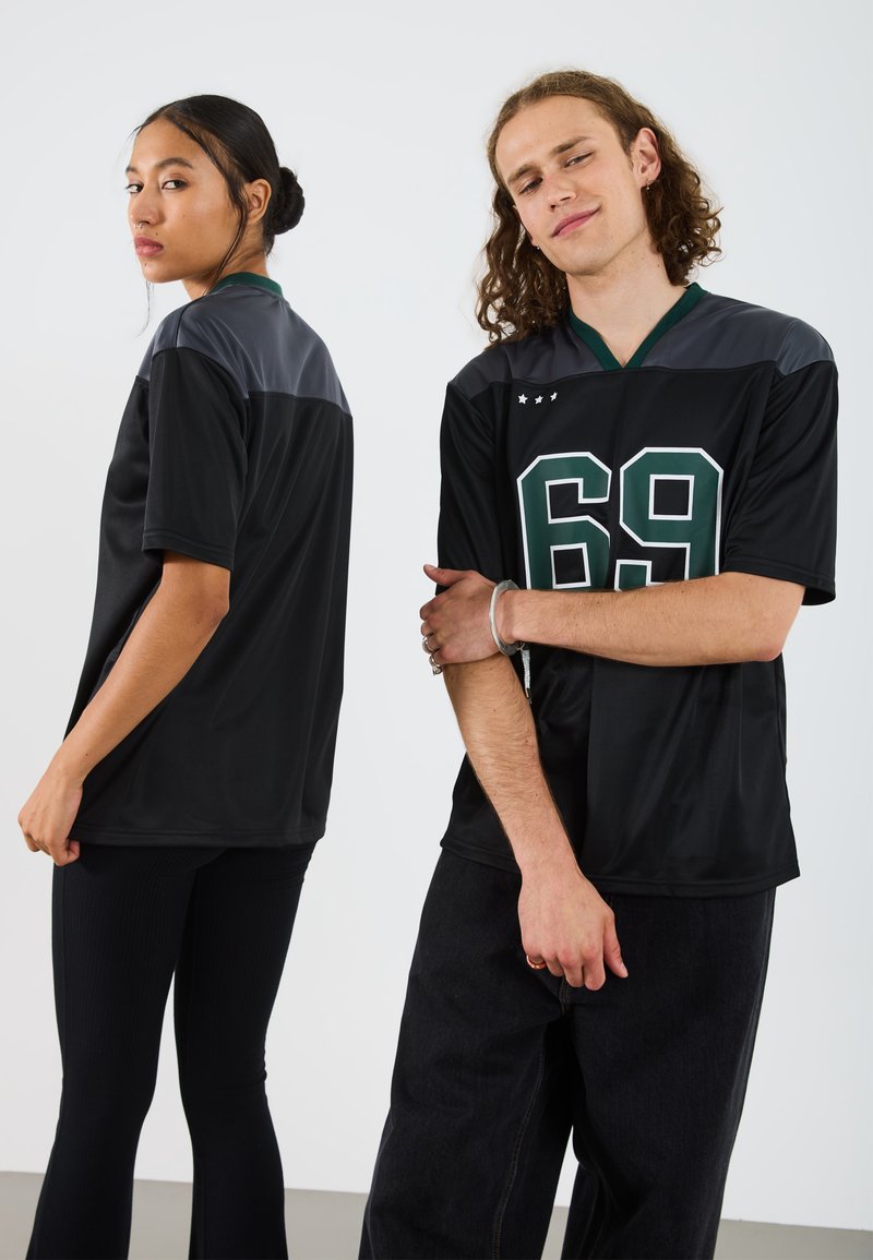 Jersey atlético negro con acentos verdes y el número 69, con mangas cortas y un escote redondeado. Paneles de hombros texturizados.