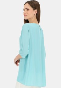 Jasnoniebieska bluzka z rękawami 3/4 i luźnym krojem. Posiada okrągły dekolt oraz pionowe rozcięcie z tyłu. Miękka, gładka struktura.
