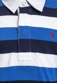 Polo con strisce larghe alternate in blu navy, bianco e blu. Realizzato in cotone con colletto bianco e dettagli del logo ricamati in rosso.