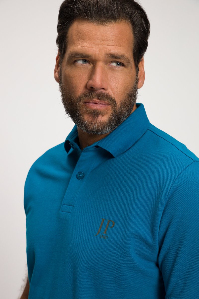 Man met baard die een blauw poloshirt met het logo "JP 1850" draagt, kijkt iets naar rechts tegen een effen achtergrond.