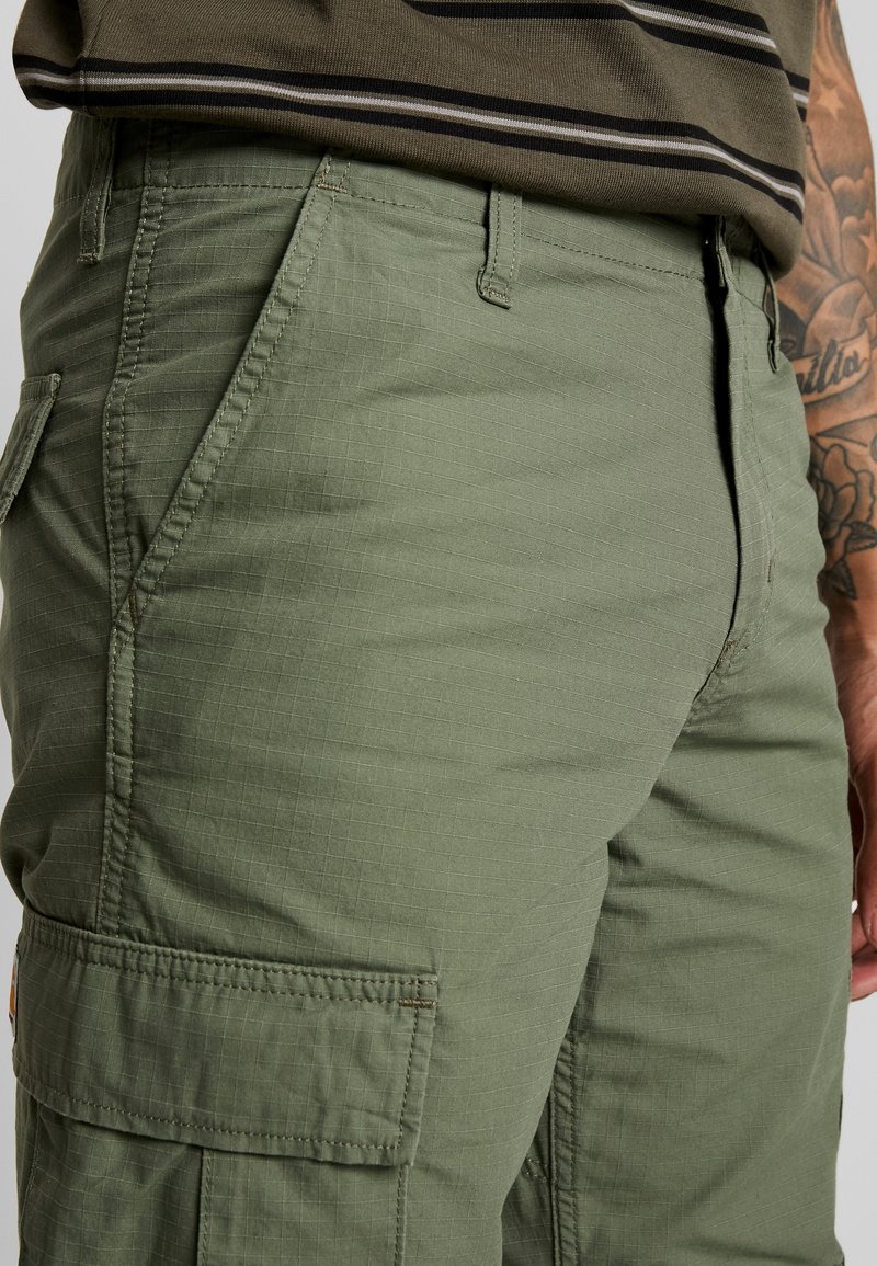 Olivengroene cargobroek van structuurstof, met zijzakken en een rechte snit. Subtiel ruitpatroon zichtbaar op het materiaal.