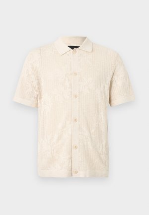 Krém csipkés rövid ujjú ing galléros nyakkivágással, virágmintával és gombos elülső résszel. Készült könnyű, texturált anyagból.