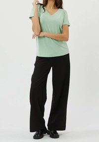 Lysegrøn kortærmet V-hals skjorte kombineret med vide sorte bukser med en glat tekstur og afslappet pasform. Sorte sko med kraftig sål.