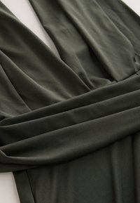 Tissu vert foncé avec des plis doux et un col en V profond, avec un détail de ceinture froncée sur un vêtement.