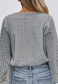 Light gray blouse featuring intricate lace detailing, long sleeves, and a relaxed fit. Material appears soft with a textured pattern.