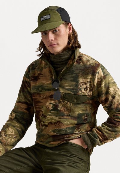 Fleece pullover in camouflage pattern with green and brown hues, featuring a high collar, buttoned chest pocket, and ribbed cuffs. Cap in olive green and black.