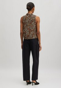 Ärmelloses Top mit Leopardenmuster in Beige und Schwarz, kombiniert mit hochgeschnittenen dunklen Hosen. Sanfte Textur, lockere Passform und minimales Ausschnittdetail.