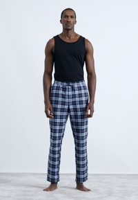 Crni top bez rukava uparen s mornarsko plavim i sivim kariranim pidžama hlačama, sa elastičnim pojasom i vezicom. Mekana tkanina, opušteni kroj.