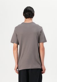 Šedé bavlněné tričko s krátkými rukávy, kulatým výstřihem a volnějším střihem. Minimalistický design bez vzorů nebo viditelných kovových detailů.