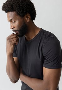 Czarny bawełniany t-shirt z krótkim rękawem, okrągłym dekoltem i teksturowanym materiałem. Zauważalny detal: mała naszywka na rękawie. Subtelna sylwetka.